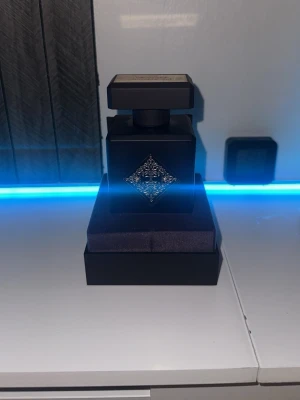 Initio High Frequency Eau de Parfum - Initio High Frequency Eau de Parfum i en lyxig svart flaska med silverdetaljer och fyrkantig form. Flaskan har en elegant dekorativ metallplatta på framsidan och kommer i en svart kartong med röd logga och mönster. Volym: 90 ml. Men är använd och finns 20-30 ml kvar 