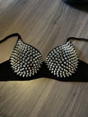 Svart bh med silverfärgade nitar - Cool svart bh dekorerad med massor av silverfärgade konformade nitar över kuporna. Bh:n har justerbara axelband. Den är förstor på mig därför jag säljer den