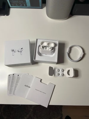 AirPods Pro - Säljer ett par vita Apple AirPods Pro med laddningsetui, extra silikonpluggar och laddningskabel. Hörlurarna har en stilren och kompakt design i plast och levereras med originalförpackning och manualer. Perfekta för dig som vill ha grymt ljud och brusreducering.