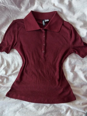 Vinröd ribbad polotopp  - Säljer en super söt ribbad polotopp från H&M med krage! Den är tunn och figur nära, på kappen står det storlek S men skulle säga att den passar mer som xs 💕