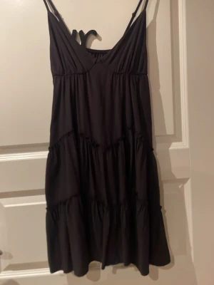 Svart ärmlös kortklänning (läs nedan för storleksbeskrivning) - Säljer en svart kortklänning med tunna axelband och volangdetaljer. Klänningen har en avslappnad passform och är perfekt för varma dagar. Tillverkad i mjukt tyg som faller snyggt. Tyvärr vet ja ej storlek men skulle säga att den är i storlek S, väldigt flowig och stretchig 
