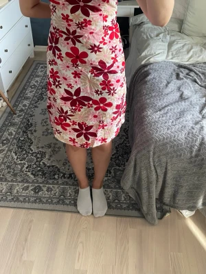 Blommig halterneck klänning röd/vit - Säljer en kort klänning med halterneck och öppen rygg. Klänningen har ett blommigt mönster i rött och vitt med inslag av rosa. Materialet känns lätt och passar perfekt till sommaren. Knyt i nacken för justerbar passform.