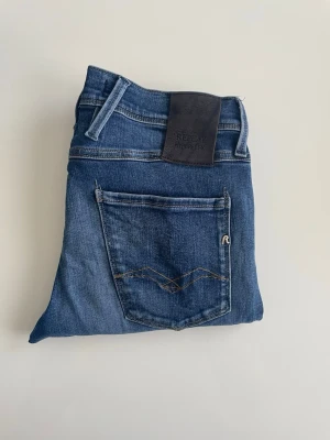 REPLAY ANBASS HYPERFLEX  - Snygga blå jeans från Replay med klassisk femficksdesign och raka ben. Jeansen har en mörkblå tvätt, kontrastsömmar och en läderpatch med Replay-logga bak i midjan. Tillverkade i slitstark denim som ger en tidlös look.