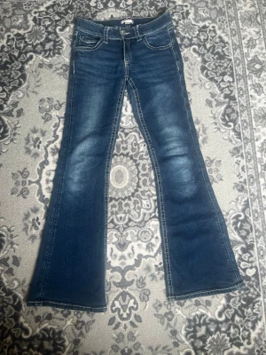 Blå bootcut jeans med broderade fickor - Säljer ett par blå bootcut jeans med vita sömmar och broderade fickor.