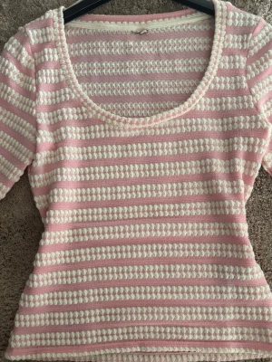Rosa och vit stickad topp - Söt stickad topp i rosa och vitt med horisontella ränder och strukturmönster. Rundad, bred ringning och halvlånga ärmar. Perfekt för dig som gillar en mjuk och retroinspirerad look. Materialet känns mjukt och stretchigt.