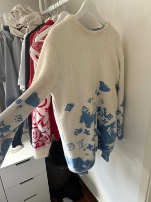 Vit och blå stickad tröja Louis Vuitton - Stickad tröja i mjukt material från Louis Vuitton. Tröjan är vit med blåa detaljer och mönster, inklusive LV-loggor och figurer. Rund halsringning och långa ärmar. Perfekt för dig som vill ha något unikt och trendigt i garderoben. ingen box o kvitto pga så pass längesen va ung då, legit checkat förr
