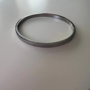 Stilrent silverfärgat armband - Snyggt och minimalistiskt armband i silverfärgad metall. Armbandet har en slät, rundad form och öppnas med ett diskret gångjärn. Perfekt för dig som gillar enkel och modern design.