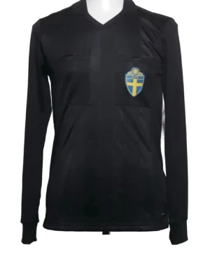 Svart långärmad domartröja SvFF - Svart långärmad domartröja med två bröstfickor och SvFF:s blågula emblem på vänster bröst. Tröjan har V-ringning och är tillverkad i ett lätt, funktionellt material som passar perfekt till fotbollsmatcher.