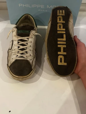 Philippe model skor - Vita sneakers med mörk mocka och gröna detaljer från Philippe Model, storlek 41 – perfekta som vardagsskor. Skorna är i bra skick och modellen är designad för att ha en lätt sliten look. Nypris ligger på 2999 kr. Tillbehör som medföljer är originalbox och digitalt kvitto.  Kolla gärna in profilen också, där finns flera märkeskläder och skor – du hittar säkert något mer som passar 😉💯 Hör av dig om du undrar något!