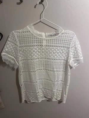 Vit spetsblus med kort ärm - Säljer en superfin vit blus i spets med korta ärmar och rund hals. Blusen har ett detaljerat spetsmönster och fransiga kanter vid ärmslut och nederkant💕