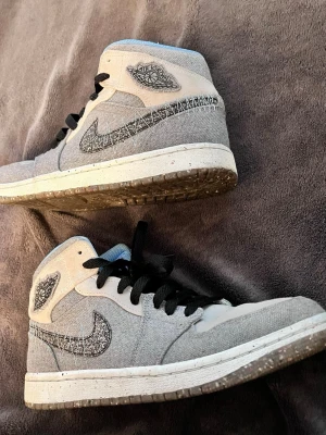 Jordan 1 mid - Snygga Nike Air Jordan 1 mi sneakers i grå canvas med svarta detaljer och broderad logga på sidan. Skorna har svart snörning, vit mellansula och prickig yttersula. Perfekta för dig som gillar streetwear och unik design. Priset kan diskuteras !