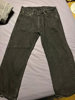 Svarta Levi's jeans - Säljer ett par svarta relaxed/loose jeans från Levi's med klassisk femficksdesign och knappgylf. Jeansen är uppsydda så de är 38/30, men känns mer som en 36a. Lite slitningar längst ner på byxorna.