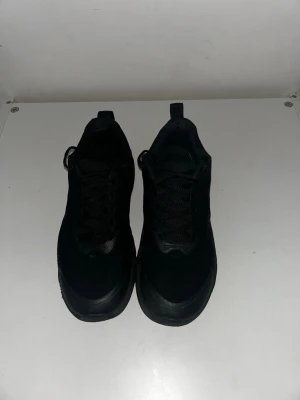 Svarta nike skor - Snygga helsvarta sneakers med klassisk låg profil och snörning. Skorna har en enkel och stilren design med rund tå och dragflik bak på hälen. Ovandelen verkar vara i textil eller syntetmaterial och sulan är i gummi. Perfekta för en clean och urban look.