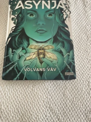 Völvans väv av Östnäs & Neidestam - Säljer boken 'Völvans väv' av Elisabeth Östnäs och Lina Neidestam. Omslaget är grönt och svart med en mystisk illustration av en kvinna och en insekt. Hårdpärm. Perfekt för dig som gillar nordisk mytologi och spännande äventyr.