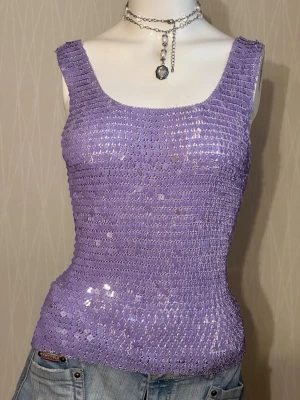 Lila paljettlinnetopp - Trendig lila linnetopp täckt med glittriga paljetter. Toppen har breda axelband, fyrkantig ringning och figurnära passform. Perfekt för dig som vill sticka ut och addera lite extra bling till din outfit.