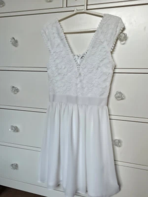 Studentklänning från nelly Vit spetsklänning med v-ringning - Superfin vit studentklänning med v-ringad spets upptill och slät kjol i lätt material. Klänningen är ärmlös och har en markerad midja. Perfekt för somriga tillfällen eller studentfirande.