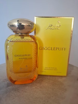 Gigglepuff Eau de Parfum 100ml - Gigglepuff Eau de Parfum från Hekayat Attar kommer i en lyxig guldfärgad flaska med gulddetaljer och matchande gul förpackning. Flaskan har en elegant, rundad form och ett stort guldfärgat lock. Innehåller 95 ml doft.