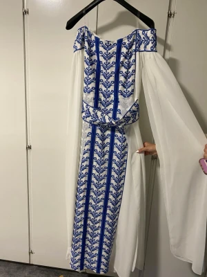 Palestinsk klänning  - En helt ny unik långklänning i vitt med blått broderat mönster och vida, transparenta ärmar. Klänningen har markerad midja och offshoulder-design. Perfekt för dig som vill sticka ut med en elegant och bohemisk stil.