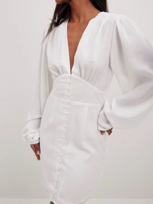 Vit studentklänning med v-ringning - Säljer min fina studentklänning som jag bara använt en gång. Likt bilden är det en vit kort klänning med djup v-ringning och långa puffärmar. Påminner om Adoores klänningar, den har markerad midja och dekorativa knappar framtill. Inte genomskinlig då det är dubbelt tyg i kjolen. Perfekt för student eller sommarens tillfällen😍 nååågot missfärgad i sömmarna på insidan, därav det billiga priset. 