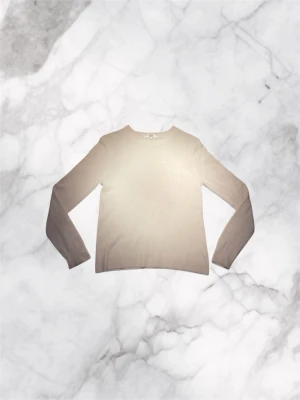 Beige cashmere tröja från Uniqlo - En 100% cashmere tröja stilren beige stickad tröja från Uniqlo med rund halsringning och långa ärmar. Tröjan har en enkel och klassisk design, perfekt för lager på lager och passar till många olika stilar. Materialet känns mjukt och bekvämt mot huden.