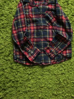 Rutig skjorta i blått och rött - Klassisk rutig skjorta i mörkblått, rött och inslag av gult. Skjortan har lång ärm, bröstficka och knappar framtill. Perfekt för en avslappnad och cool stil.