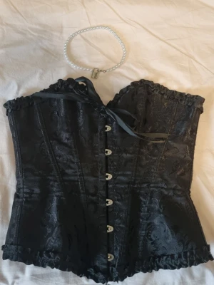 Svart korsett med rosett - Svart gothic viktoriansk stil korsett, genuint det vackraste jag äger börjar snart gråta asså. Kom aldrig till användning. Fina rosetter och volangdetaljer.