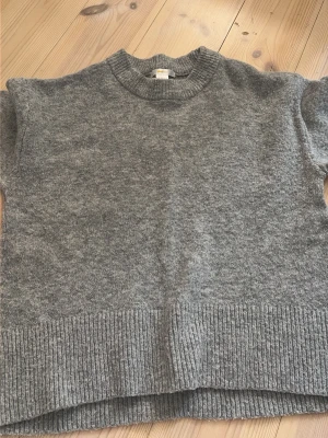 Grå stickad tröja Gina Tricot - Mysig grå stickad tröja från Gina Tricot med rund halsringning och bred ribbad kant nedtill. Tröjan har en rak passform och kortare ärmar, perfekt för lager på lager. Enkel och stilren design som passar till det mesta.