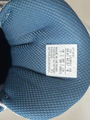 Vita och blå Asics sneakers - Snygga vita sneakers från Asics med blå detaljer och klassiska ränder på sidorna. Ovandelen är i mesh och syntet för bra andningsförmåga och komfort. Skorna har vita snören och en vadderad plös och krage för extra support.