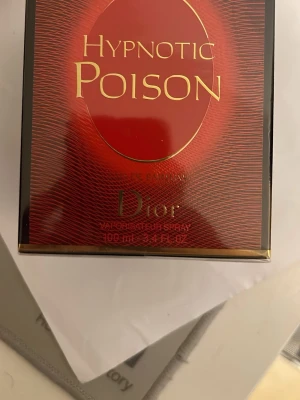 Dior Hypnotic Poison EdP 100ml - Säljer en lyxig parfym, Hypnotic Poison Eau de Parfum från Dior. Flaskan rymmer 100 ml och kommer i en elegant röd och svart förpackning med guldiga detaljer. Doften är känd för sin intensiva och sensuella karaktär, perfekt för dig som vill sticka ut.
