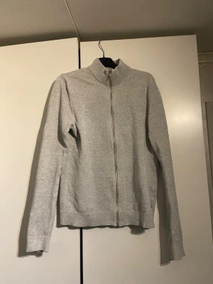 Ljusgrå ziptröja med hög krage - En stilren ljusgrå ziptröja med hög krage och långa ärmar. Tröjan har ribbade muddar vid ärmslut och nederkant samt dragkedja framtill. Perfekt för lager på lager och enkel att matcha med olika outfits.         Den är xs men har passat mig fram till 178 längd. Slim fit passform
