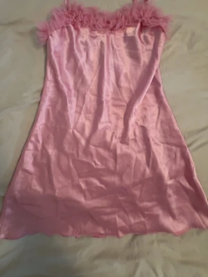 Rosa nattklänning  - Sött nattklänning i glansigt rosa satin med tunna axelband och volangkant upptill. Materialet känns mjukt och lyxigt mot huden och volangerna ger en romantisk touch. Perfekt för dig som gillar en feminin och bekväm stil när du ska sova.