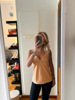 Ljusrosa spetsdetaljerad linnetopp - Söt ljusrosa linnetopp med breda axelband och v-ringning. Toppen har fina spetsdetaljer längs midjan, axelbanden och nederkanten som ger en romantisk vibe. Perfekt till jeans eller kjol för en fräsch look. Färgen liknar mest bild 1! 