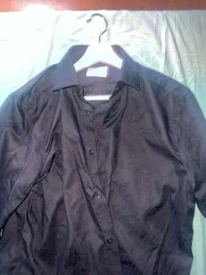 Svart skjorta med knappar från dressman, Använd en gång och köpt i januari. - Stilren svart skjorta med klassisk krage och knäppning framtill. Skjortan har lång ärm och är tillverkad i ett slätt tyg som ger en snygg look. Perfekt för dig som gillar en enkel men ändå elegant stil.