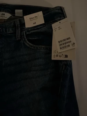 Blå slim fit jeans från H&M - Säljer ett par blå slim fit jeans från H&M med klassisk femficksmodell och normalhög midja. Jeansen har bälteshällor och dragkedjegylf. Perfekta för dig som gillar en smalare passform och tidlös denimstil.