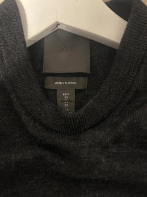 Mörkgrå merinoullströja från H&M - Snygg mörkgrå stickad tröja från H&M i mjuk merinoull. Tröjan har rund halsringning, långa ärmar och en klassisk, smal passform. Perfekt för lager-på-lager och enkel att matcha med olika stilar.