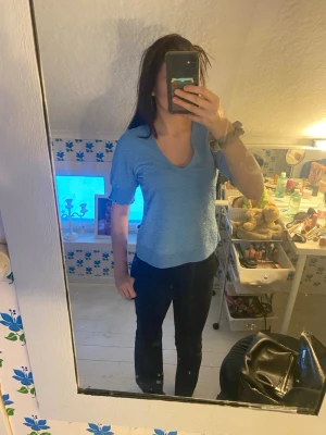 Blå v-ringad topp med korta ärmar - Säljer en ljusblå topp med v-ringning och korta ärmar. Toppens material är troligtvis bomull eller polyester och den har en normal passning. Perfekt för dig som gillar enkel och stilren design.