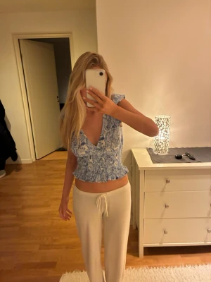 Blommig blå och vit blus från Ginatricot - Supersöt blommig blus från Ginatricot i blått och vitt. Toppen har v-ringning, korta ärmar och smockad midja med volangkant. Perfekt för en fräsch och somrig look. Lätt och luftig i bomullsmix.