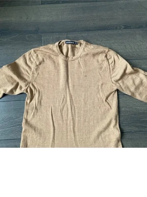 Beige stickad tröja från J.Lindeberg - Säljer en stilren beige stickad tröja från J.Lindeberg med diskret broderad logotyp på bröstet. Tröjan har rund hals och långa ärmar, perfekt för lager-på-lager och enkel att matcha till! Ordinarie pris 1600kr