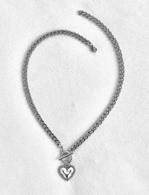 Silverfärgat halsband med hjärthänge - Snyggt halsband i silverfärgad metall med en kedja och ett hjärthänge. Halsbandet har ett dekorativt toggle-lås framtill som ger en cool detalj. Hjärtat har en blank yta och en ram med små kulor runt om. Perfekt accessoar för att lyfta din outfit.