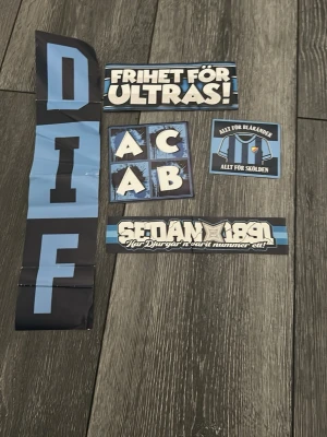 DIF klistermärken ultras supporter - Ett set med flera klistermärken i blått, svart och vitt med DIF-tema. Innehåller texter som 'FRIHET FÖR ULTRAS!', 'SEDAN 1891', 'ALLT FÖR BLÅRANDER', samt stora bokstäver och supporterbudskap. Perfekt för dig som vill visa ditt stöd för Djurgården.