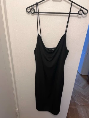 Svart kort klänning  - Säljer en svart kort klänning från bik bok med tunna axelband och draperad urringning. Klänningen har en enkel och stilren design som passar perfekt till många olika tillfällen. Materialet känns mjukt och följsamt mot kroppen.