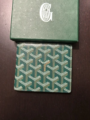 Grön plånbok från Grischyard - Stilren grön plånbok från Garo med präglat mönster och silverfärgad logotyp på framsidan. Plånboken har en rektangulär form och är tillverkad i ett tåligt material som ger en exklusiv känsla. Perfekt för dig som vill ha något unikt och snyggt i fickan.