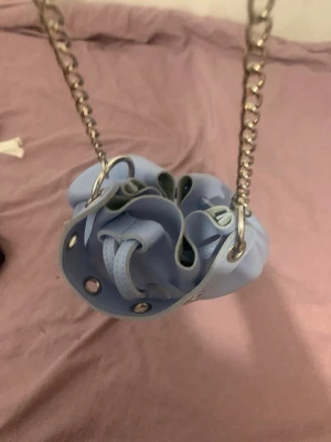 Ljusblå bucket bag med kedjerem - Söt ljusblå handväska i bucket-modell med dragsko och silverfärgade metalldetaljer. Väskan har en kedjerem som ger en cool touch och är gjord i ett slätt, mjukt material. Perfekt för dig som vill ha en trendig och unik accessoar.