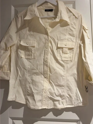 Vit skjorta från Lindex med fickor - Klassisk vit skjorta från Lindex med krage, knappar framtill och två bröstfickor med lock. Skjortan har trekvartsärm och är tillverkad i bomull för en skön känsla. Perfekt till jeans eller kjol för en clean look.