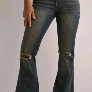 Blå bootcut jeans med slitningar från true religion - Säljer ett par blå bootcut jeans med slitningar vid knäna och klassisk femficksdesign. Jeansen har en snygg tvätt och vida ben. Storlek 25, midjemått: ca 35 cm rakt över, Innerbenslängd: 76 cm