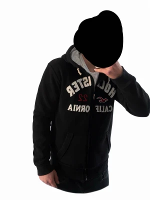  Hollister hoodie  - Det Svart hoodie från Hollister med vit dragkedja och stora broderade bokstäver på bröstet. Har huva med vita snören och mjukt grått innerfoder. Framfickor och ribbade muddar. Klassisk streetstil med trycket 'California 22' och Hollister-logga. Den är i storlek xxl men jag skulle säga M/S Modellen är 181 cm lång.   Pris kan diskuteras vid snabb affär!