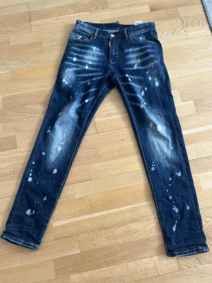 Mörkblå jeans med blekta detaljer - Snygga mörkblå jeans med unika blekta och stänkta detaljer framtill och baktill. Klassisk femficksmodell med raka ben och orange sömmar. Perfekta för dig som gillar en lite mer edgy och avslappnad stil.