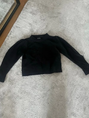 Svart stickad tröja med puffärm - Trendig svart stickad tröja med puffärmar och ribbade muddar vid ärmslut och nederkant. Kortare modell som passar perfekt till höga jeans eller kjol. Mjuk och skön, perfekt för kyligare dagar. I storlek L från Lindex!! 💕