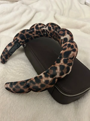 Leopardmönstrat vadderat diadem - Säljer ett trendigt diadem med leopardmönster i beige, brunt och svart. Diademet är vadderat och har en vågig form som ger extra volym och attityd till din look. Perfekt accessoar för att sticka ut och ge outfiten en cool touch.