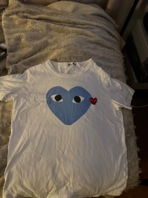 Vit Comme des Garçons PLAY t-shirt - Säljer Comme des Garçons PLAY t-shirt – vit med blått hjärta  Nu säljer jag min stilrena och populära t-shirt från Comme des Garçons PLAY. Vit modell med det klassiska blå hjärtat och små röda hjärtat upptill framtill. En tidlös och snygg design som passar till allt. 	•	Märke: Comme des Garçons PLAY 	•	Färg: Vit 	•	Tryck: Blått hjärta med ögon + rött hjärta 	•	Skick: (ganska bra ) 	•	Storlek: (S)  Perfekt både till vardag och mer uppklädda outfit